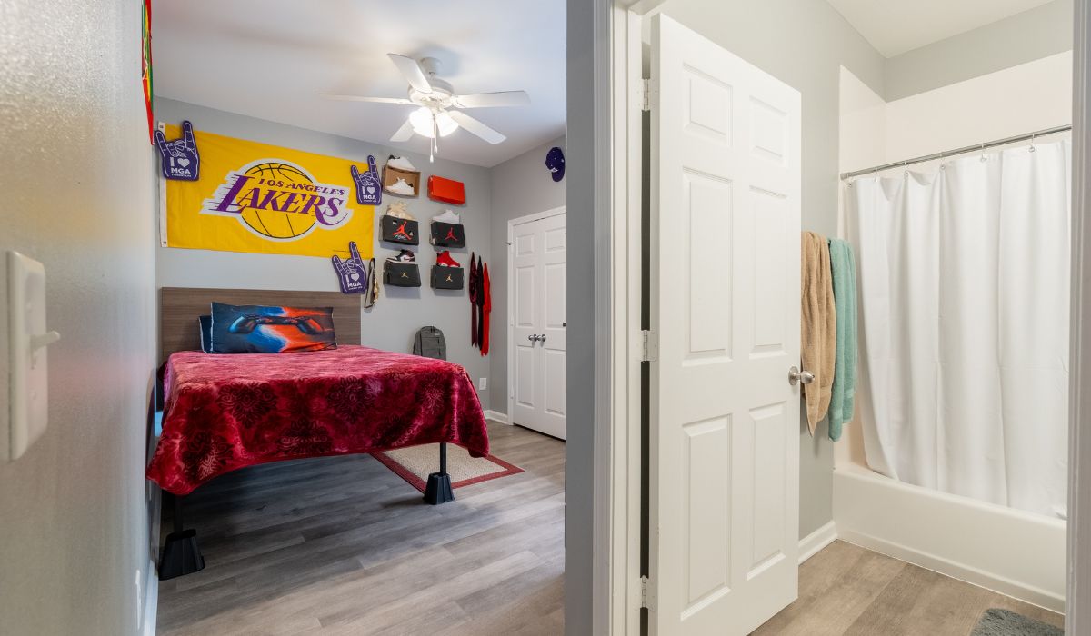 A bedroom with a Lakers poster above it and a bathroom within the bedroom.